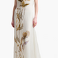 A woman wearing the Altuzarra Jools Dress, a sleeveless, floor-length silk gown featuring a bold, realistic thistle flower print on the front.
