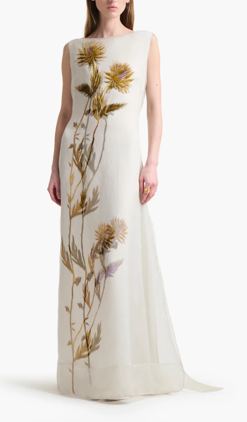 A woman wearing the Altuzarra Jools Dress, a sleeveless, floor-length silk gown featuring a bold, realistic thistle flower print on the front.