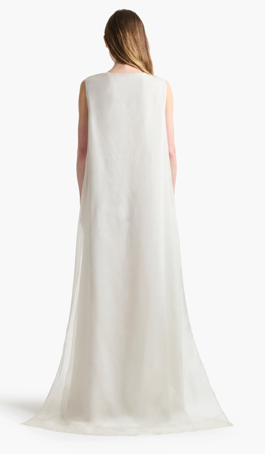 A person with long hair stands with their back to the camera, wearing Altuzarra's floor-length, sleeveless white silk Jools Dress.