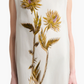 A woman wears the Altuzarra Jools Dress, a sleeveless ivory silk piece adorned with embroidered thistle flowers and green stems.