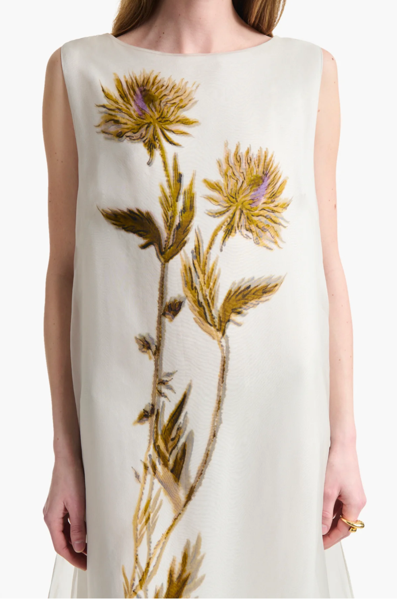 A woman wears the Altuzarra Jools Dress, a sleeveless ivory silk piece adorned with embroidered thistle flowers and green stems.