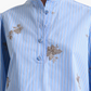 A person wearing the Margot Top by Altuzarra, a modern light blue cotton-poplin shirt featuring a mandarin collar, button placket, balloon sleeves, and floral embroidery.
