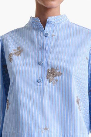 A person wearing the Margot Top by Altuzarra, a modern light blue cotton-poplin shirt featuring a mandarin collar, button placket, balloon sleeves, and floral embroidery.