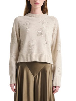 A woman wears the Altuzarra Paulie Sweater, a cream long-sleeve virgin wool top with raised floral embroidery, styled with an olive satin skirt.