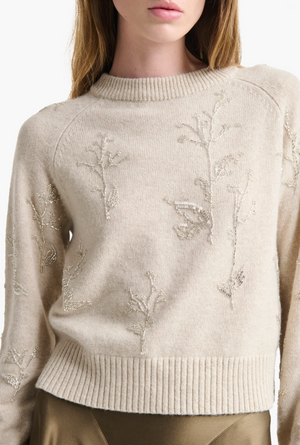 A woman wears the Altuzarra Paulie Sweater, crafted from cream virgin wool with embroidered floral patterns, beaded embellishments, and ribbed collar and hem.