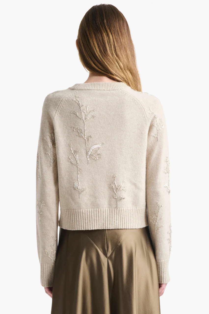 A person with long hair wears the Altuzarra Paulie Sweater, featuring delicate floral embroidery and beads, styled with a khaki skirt and photographed from behind against a plain background.
