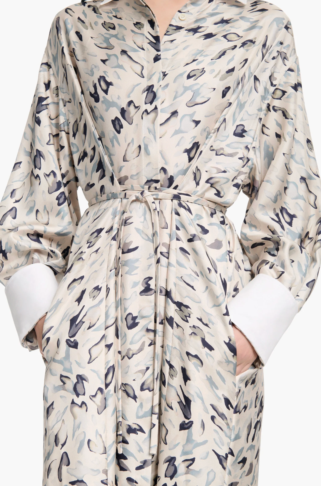 A person wearing the Altuzarra Floyd Dress—featuring a light-colored, abstract animal pattern, white cuffs, a tied waist, and pockets.