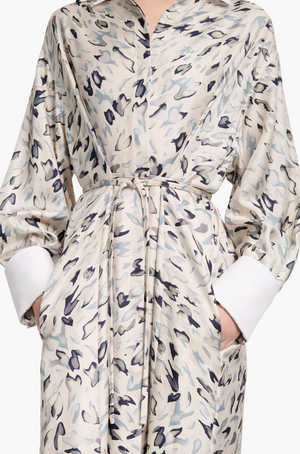 A person wearing the Altuzarra Floyd Dress—featuring a light-colored, abstract animal pattern, white cuffs, a tied waist, and pockets.