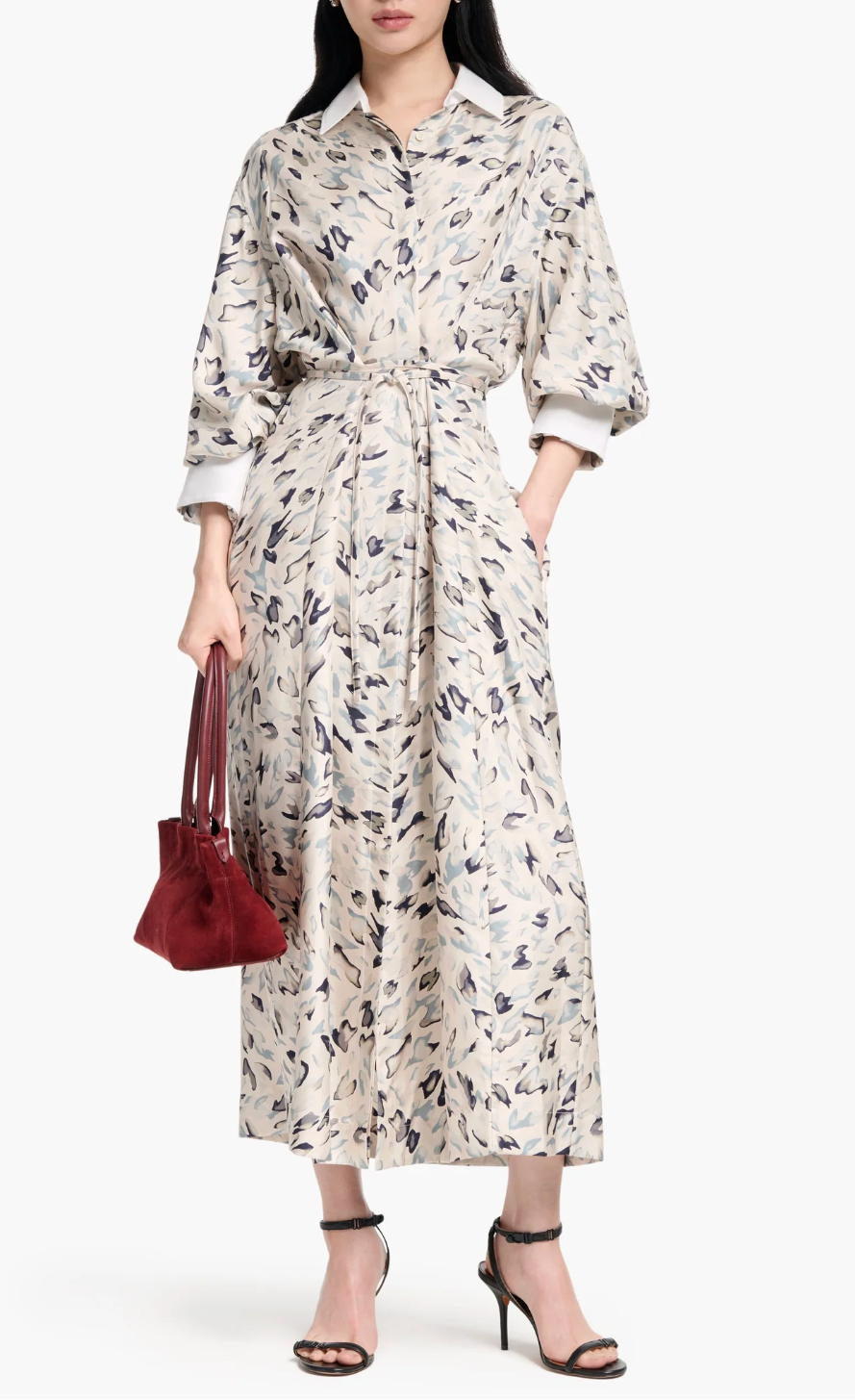 Someone in the Altuzarra Floyd Dress, styled with a shirt silhouette and belted waist, paired with black high-heeled sandals and a small red handbag.