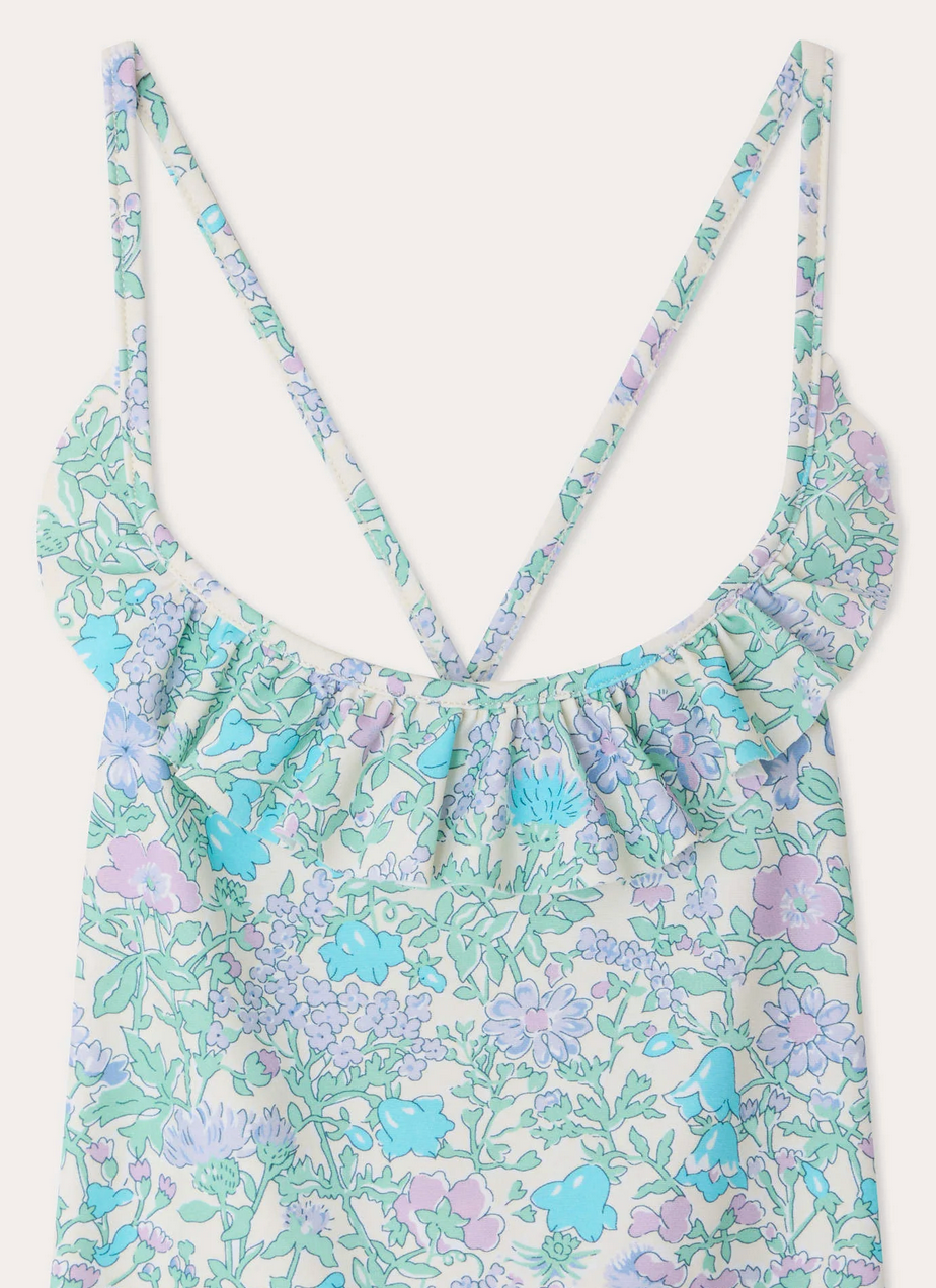 Close-up of Bonpoint's Girls' Lacy One Piece Swimsuit with a floral print in pastel purple, blue, and green, featuring thin shoulder straps and a ruffled neckline crafted from Liberty fabric.
