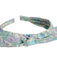 The Girls' Lorette Headband by Bonpoint features a stylish front knot and is crafted from pastel green, purple, and blue Liberty floral fabric.