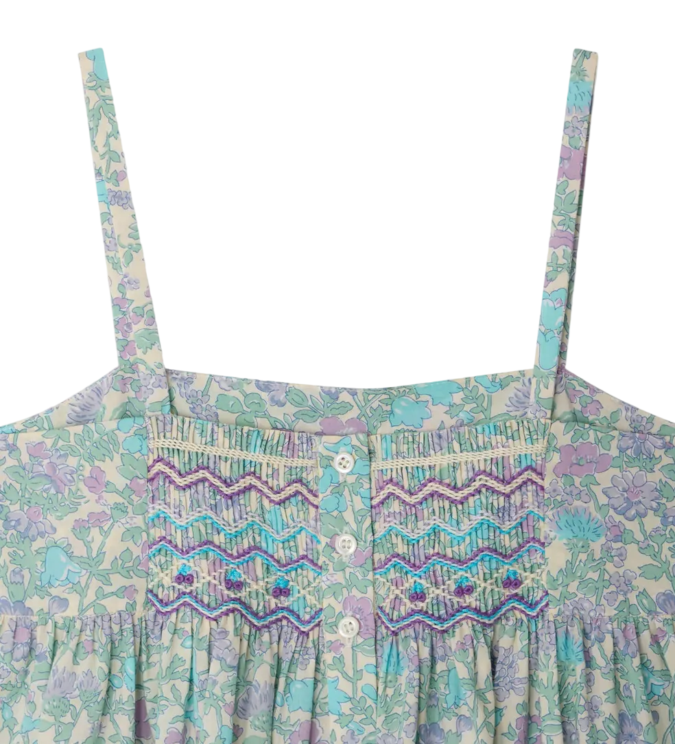 Close-up of the Bonpoint Girls' Passion Dress bodice: Liberty floral fabric, thin straps, hand-embroidered smocking with purple and blue stitching, and three white center buttons.