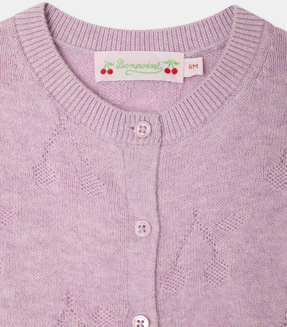Closeup of the Girls' Teyana Cardigan by Bonpoint, in light purple soft knit with a round neckline, ribbed trim, and four buttons. Made from organic cotton. The label features cherries and size 6M.