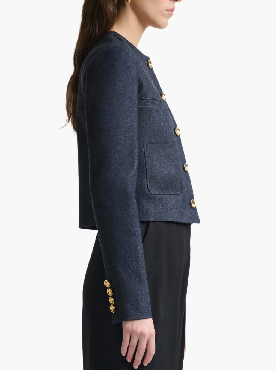 A woman is shown from the side wearing Altuzarra's Bernadette Jacket in dark blue with gold buttons and patch pockets, paired with black pants, set against a plain background.