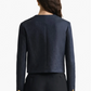 A woman is shown from the back wearing the Altuzarra Bernadette Jacket, a navy cropped blazer with gold sleeve buttons and a slim fit, paired with black trousers.
