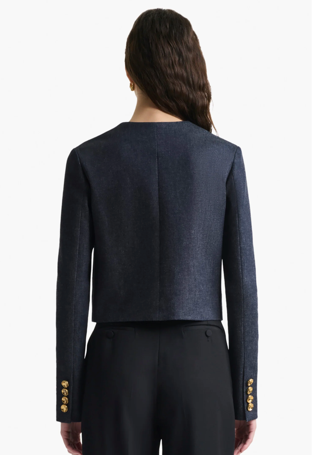 A woman is shown from the back wearing the Altuzarra Bernadette Jacket, a navy cropped blazer with gold sleeve buttons and a slim fit, paired with black trousers.