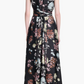 A woman faces away, wearing the Altuzarra Penny Dress—a sleeveless, floor-length black floral dress with a tied waist, ideal for elegant wedding guest attire.