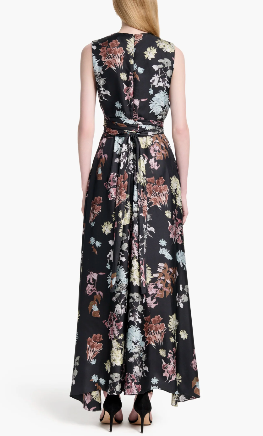 A woman faces away, wearing the Altuzarra Penny Dress—a sleeveless, floor-length black floral dress with a tied waist, ideal for elegant wedding guest attire.