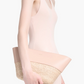 A woman in a sleeveless pale pink dress holds the Altuzarra Basket Clutch, a blush pink woven leather accessory, against a plain white background.