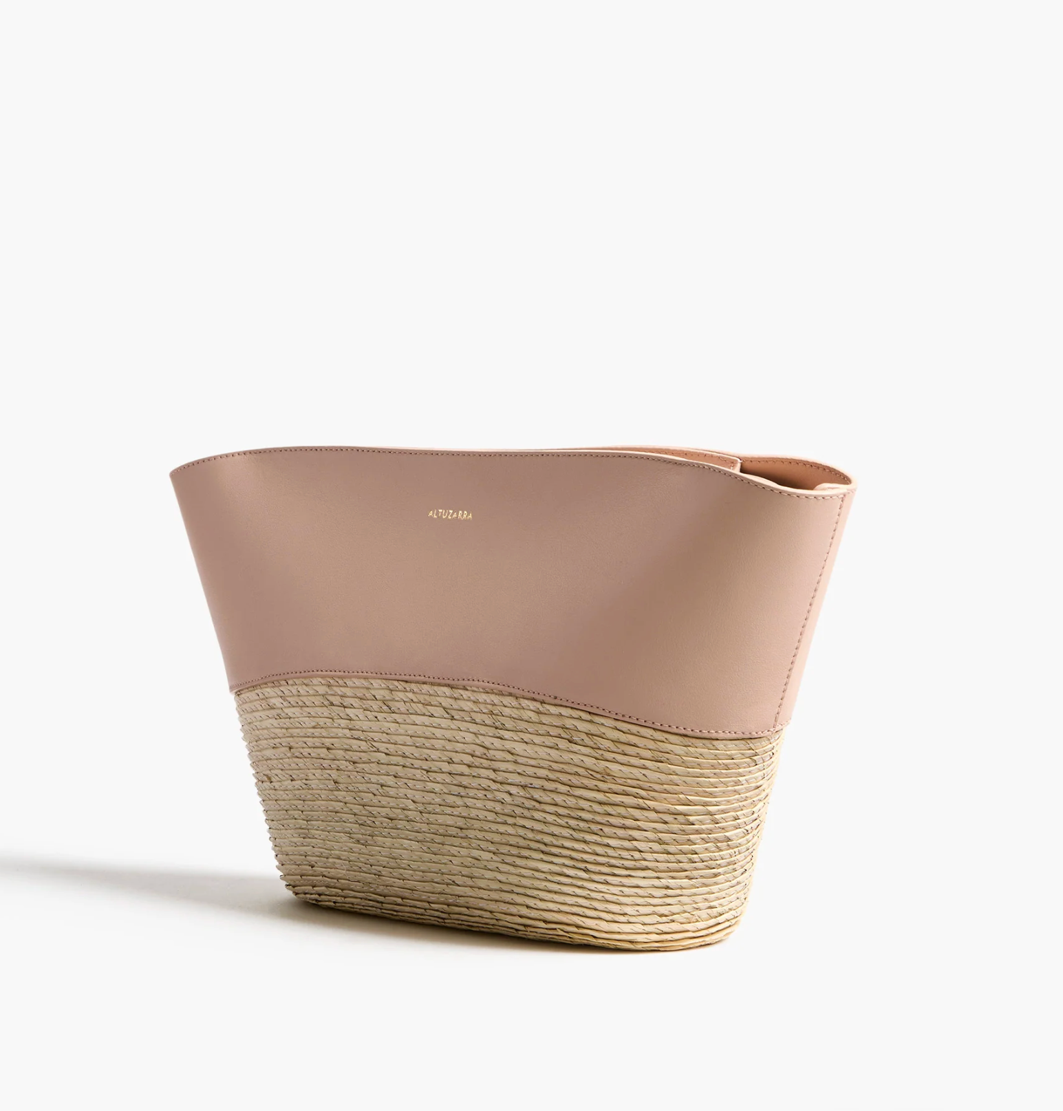 The Altuzarra Basket Clutch features a blush pink leather upper, woven straw lower section, minimalist design, and a subtle gold logo on the leather.