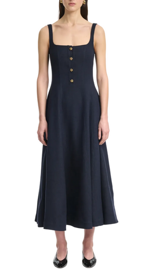 A woman in the Altuzarra Orrie Dress—a sleeveless, navy A-line midi in linen blend with a square neckline and vintage-style front buttons—paired with black flats.
