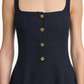 A woman wears the Altuzarra Orrie Dress—a sleeveless, square-neck navy linen-blend style featuring four vintage-inspired gold buttons down the front.
