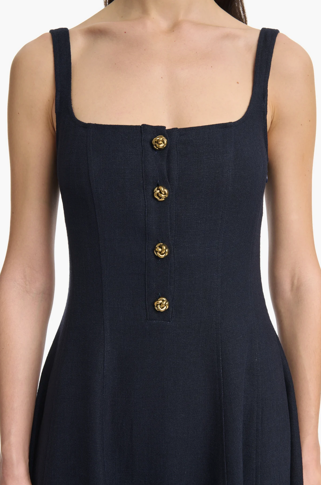 A woman wears the Altuzarra Orrie Dress—a sleeveless, square-neck navy linen-blend style featuring four vintage-inspired gold buttons down the front.