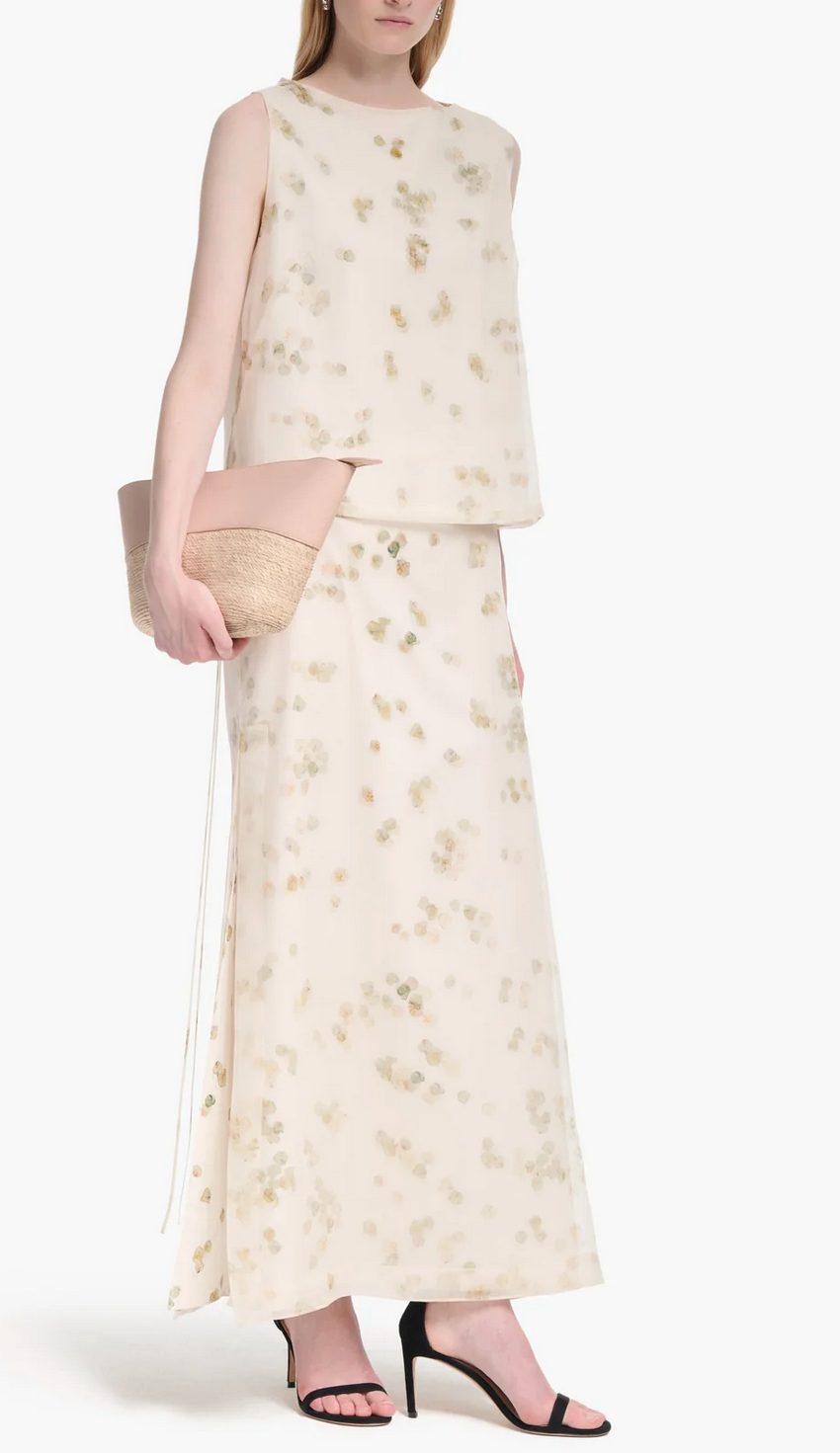 A woman wears the Altuzarra Linnie Skirt—a cream maxi with subtle petal motifs—paired with a matching sleeveless top, beige clutch, and black heeled sandals.