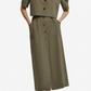 Wearing the Blaze Milano Midday Sun Nija Skirt in palm green linen, paired with a button-down, short-sleeve cropped jacket, hands in pockets and gray flats.