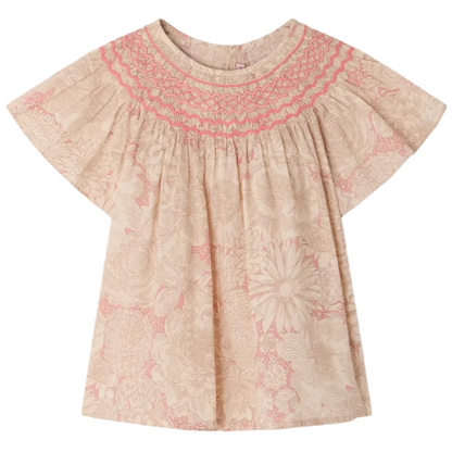 The Bonpoint Girls' Adelice Blouse features short sleeves, cream Liberty fabric with a pink floral pattern, and hand-embroidered smocked detailing at the neckline.