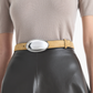 Person wearing a beige short-sleeve top, an Altuzarra Oval Plaque Belt in tan calf leather with a silver-tone metal buckle, and a black leather skirt.