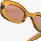 Close-up of Jimmy Fairly’s Cinnamon sunglasses, featuring an oval frame in amber cellulose acetate with brownish lenses and sturdy metal hinges, set against a plain white background.