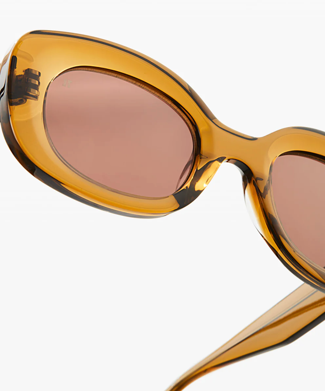 Close-up of Jimmy Fairly’s Cinnamon sunglasses, featuring an oval frame in amber cellulose acetate with brownish lenses and sturdy metal hinges, set against a plain white background.