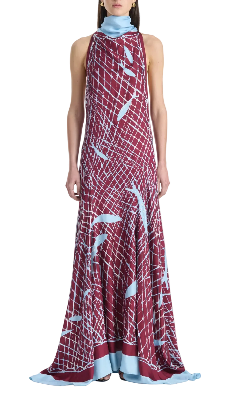 A woman wears the Moonlight Dress by Altuzarra, a sleeveless, floor-length maroon silk dress adorned with a light blue grid and abstract pattern, featuring a high neck and a light blue hem.