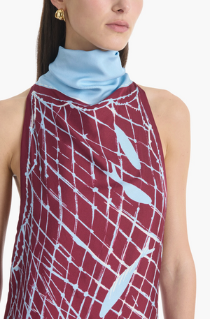 A woman wearing the Altuzarra Moonlight Dress, a sleeveless burgundy piece featuring light blue abstract patterns and a high neckline accented with a light blue scarf-like collar.
