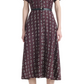 A woman wears the Altuzarra Kiera Dress, a knee-length, short-sleeved maroon pure silk dress featuring a geometric white pattern, cinched at the waist with a leather belt and paired with black strappy heels.