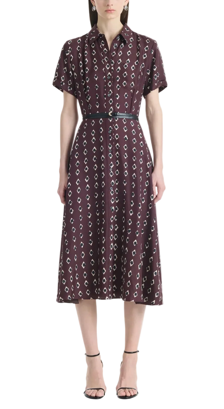 A woman wears the Altuzarra Kiera Dress, a knee-length, short-sleeved maroon pure silk dress featuring a geometric white pattern, cinched at the waist with a leather belt and paired with black strappy heels.