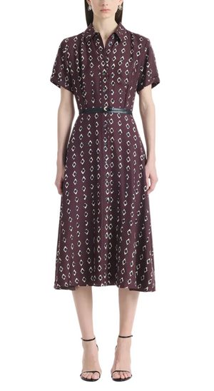 A woman wears the Altuzarra Kiera Dress, a knee-length, short-sleeved maroon pure silk dress featuring a geometric white pattern, cinched at the waist with a leather belt and paired with black strappy heels.