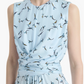 A woman wearing the Altuzarra Penny Dress, a sleeveless light blue silk dress featuring a bird print pattern, gathered waist detail, and an elegant asymmetric hem.