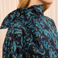 A woman wearing the Ulla Johnson Pastel Long Sleeve Cotton Blouse stands in front of a cream-colored background, featuring a high-neck with a tied bow, long sleeves, and a blue and green floral design that creates an elegant, structured silhouette.