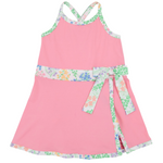 Girls’ Prepletic™ Teggy Tennis Dress by The Beaufort Bonnet Company—a pink sleeveless dress with a floral trim and matching waist sash, featuring a crossover back and floral edging at the hem and neckline for a playful yet polished activewear-inspired look.