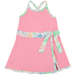 Girls’ Prepletic™ Teggy Tennis Dress by The Beaufort Bonnet Company—a pink sleeveless dress with a floral trim and matching waist sash, featuring a crossover back and floral edging at the hem and neckline for a playful yet polished activewear-inspired look.
