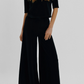 A person wearing a short-sleeved black top and black Suzie Kondi Megalo Velour Pants with a front seam.