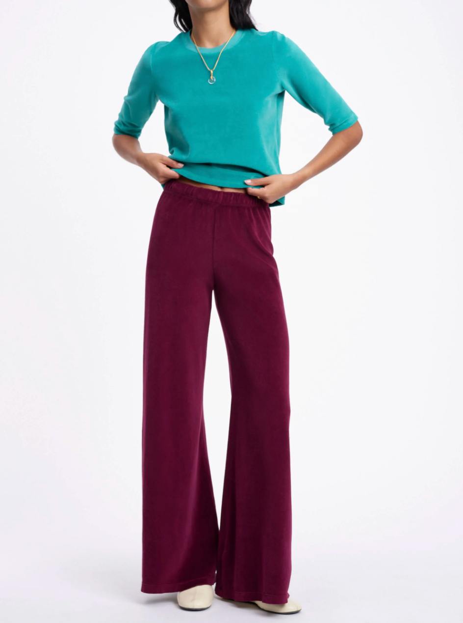 A person wearing a teal short-sleeved top and dark red wide-leg Suzie Kondi Zephyra Velour Pants.