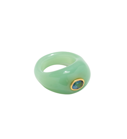 The Lizzie Fortunato Monument Ring by Lizzie Fortunato, featuring a mint green jade centerpiece set in gold and adorned with a small blue gemstone, is showcased on a white background, exemplifying colorful wearable art.