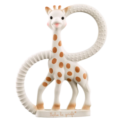 A charming toy giraffe from Sophie la Girafe, crafted from natural rubber with brown spots, stands on a base while holding the Teething Ring, which is adorned with textured surfaces.