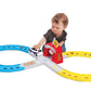 A young child plays with a Maisto Shake-it Runner Infinity Track, a figure-eight toy car racetrack featuring blue and yellow tracks, a small red tunnel, and plenty of space for emergency vehicle toys to zoom around.