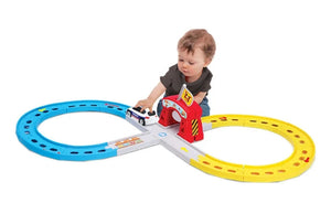 A young child plays with a Maisto Shake-it Runner Infinity Track, a figure-eight toy car racetrack featuring blue and yellow tracks, a small red tunnel, and plenty of space for emergency vehicle toys to zoom around.