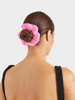 A woman with brown hair in a neat bun, secured by a Hunza G Scrunchie, wears a sleeveless black textured top and is shown from the back against a plain light background.
