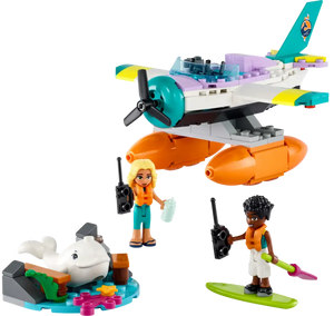 Two LEGO Friends figures, one blonde with a map and the other with dark curly hair holding a paddle, stand by the LEGO® Friends Sea Rescue Plane from Legos - Toyhouse. Nearby, a dolphin figure rests on blue LEGO pieces from this building toy set.